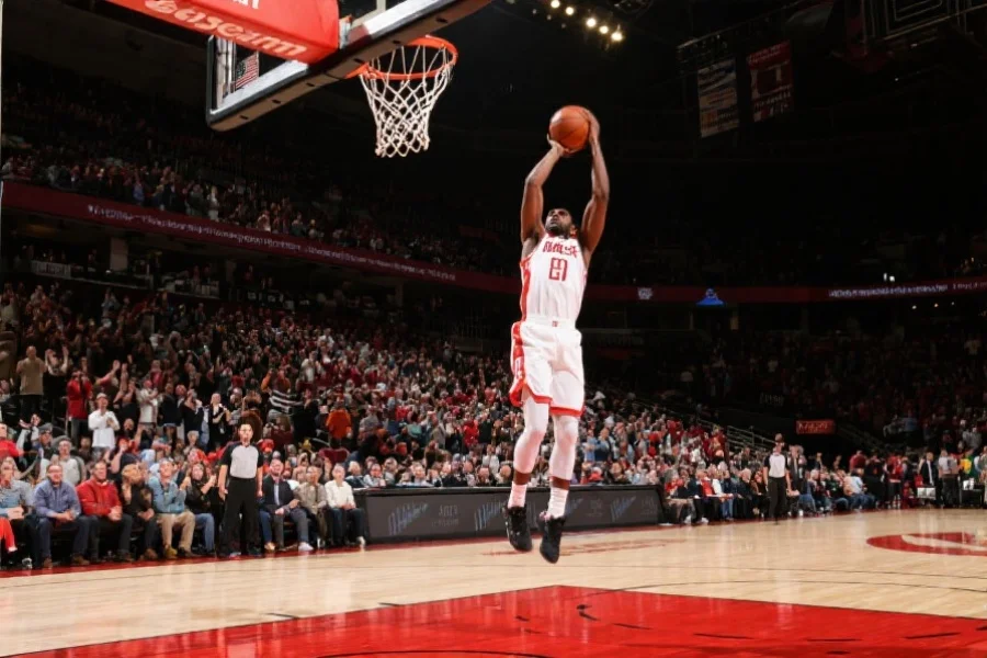 篮球运动员在球场上高高跃起，准备扣篮，观众席上气氛热烈